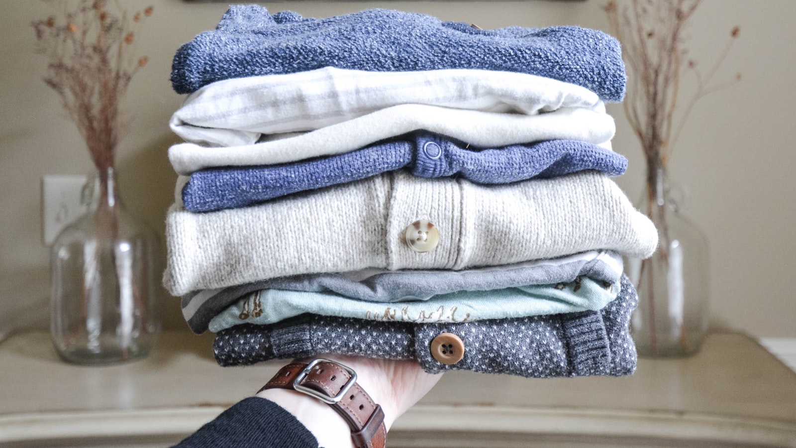 Hand hält einen Stapel gefalteter Kleidung zum Weitergeben und Spenden