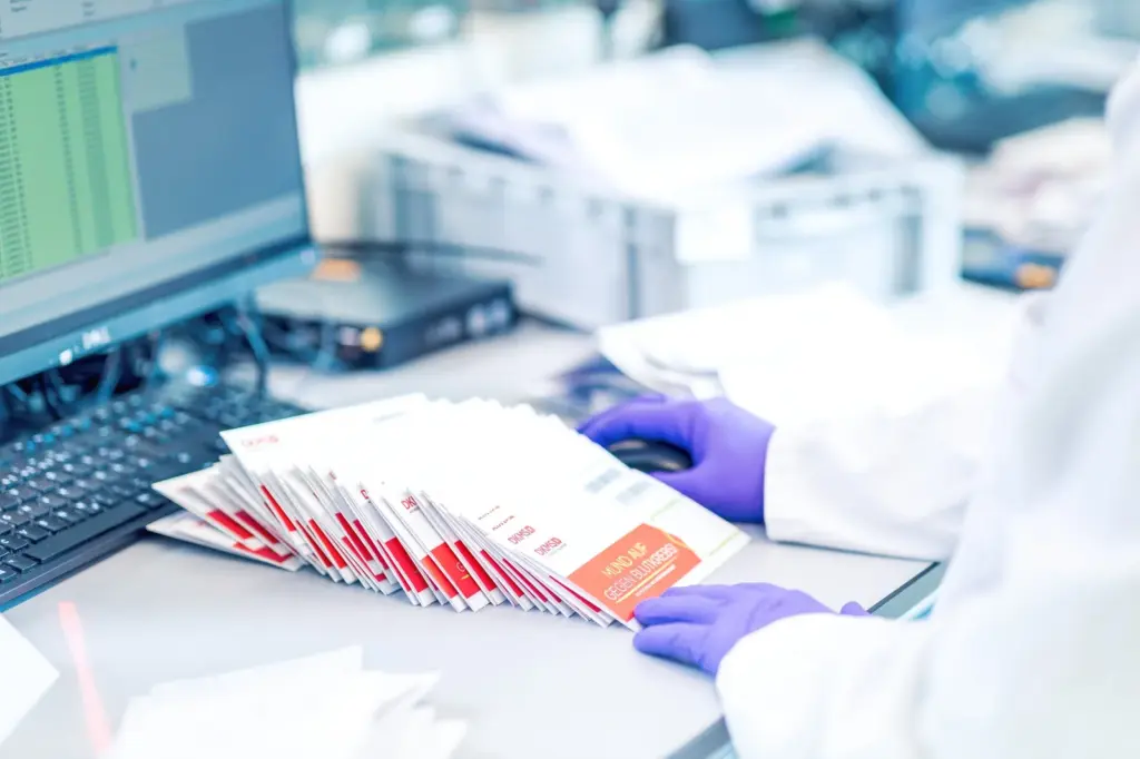 Mitarbeiterin im Labor bearbeitet Registrierungsunterlagen der DKMS an einem Schreibtisch.
