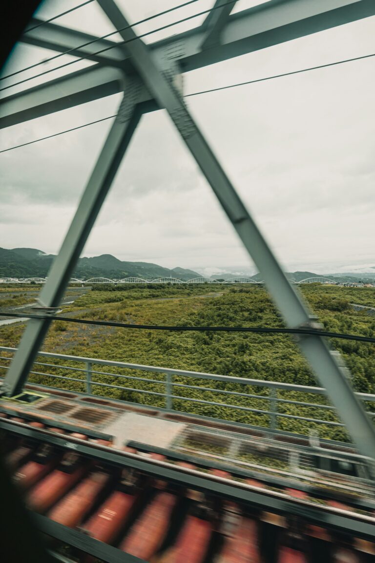 Blick aus dem Zugfenster auf grüne Hügellandschaft und Felder – typische Slow Travel Atmosphäre beim Bahnreisen durch Europa