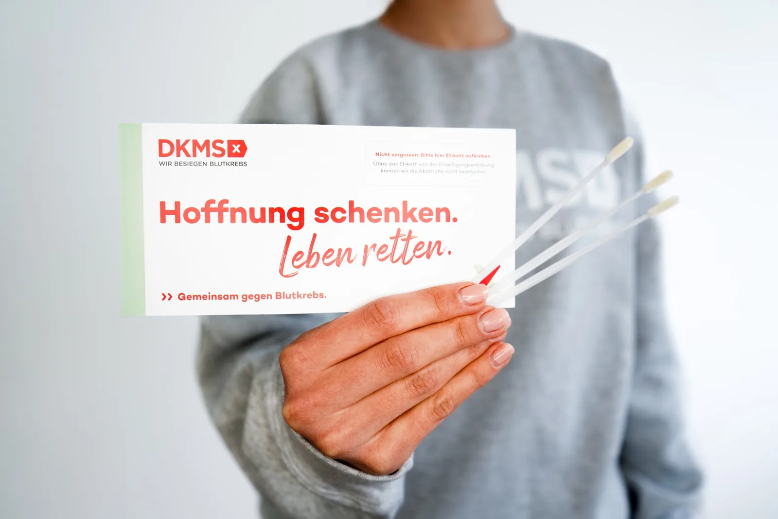 Person hält ein DKMS-Registrierungsset mit Wattestäbchen zur Stammzellspende in der Hand.
