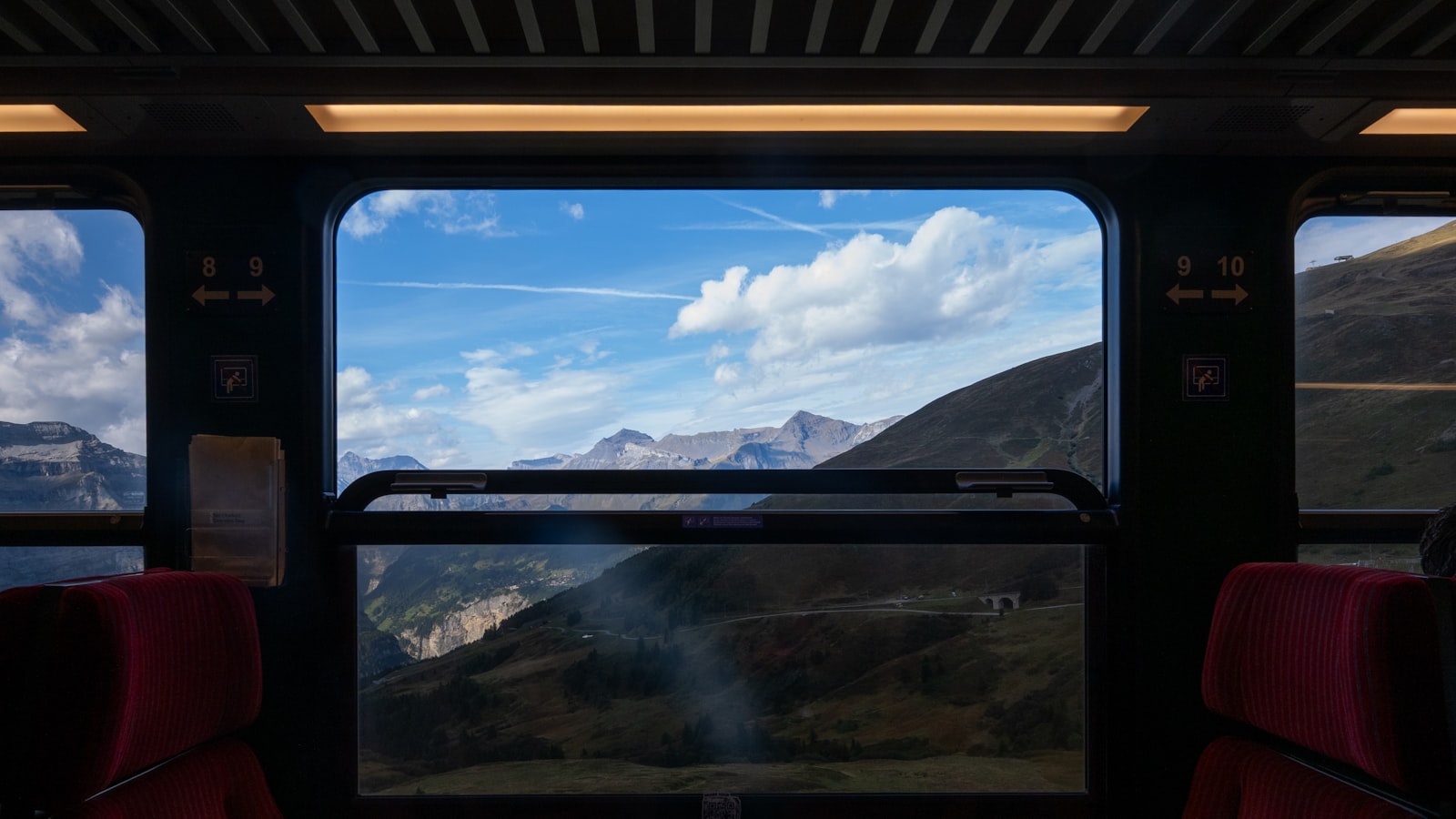 Blick durch ein Zugfenster auf eine Berglandschaft unter blauem Himmel – Bahnreise durch Europa