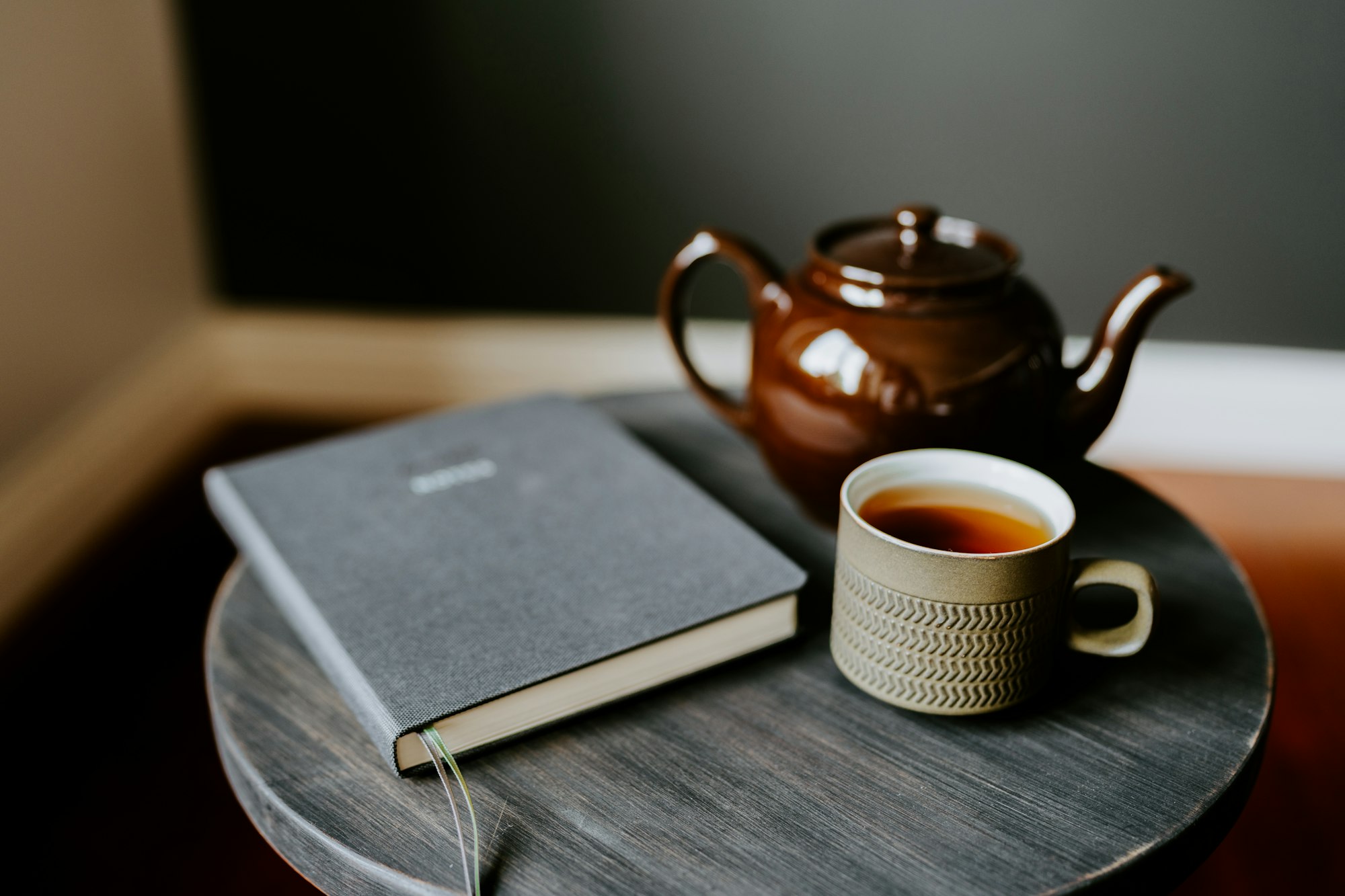 Eine Tasse Tee und ein aufgeschlagenes Buch auf einem Holztisch im warmen Morgenlicht