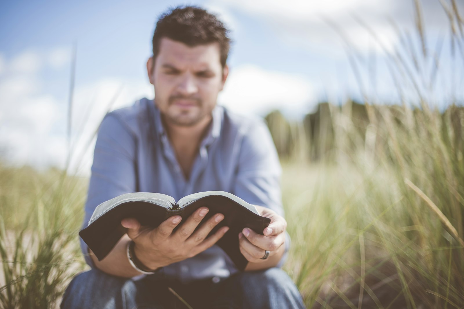 Mann liegt im Gras auf einer Wiese und liest entspannt ein Buch – analoge Auszeit in der Natur ohne Smartphone