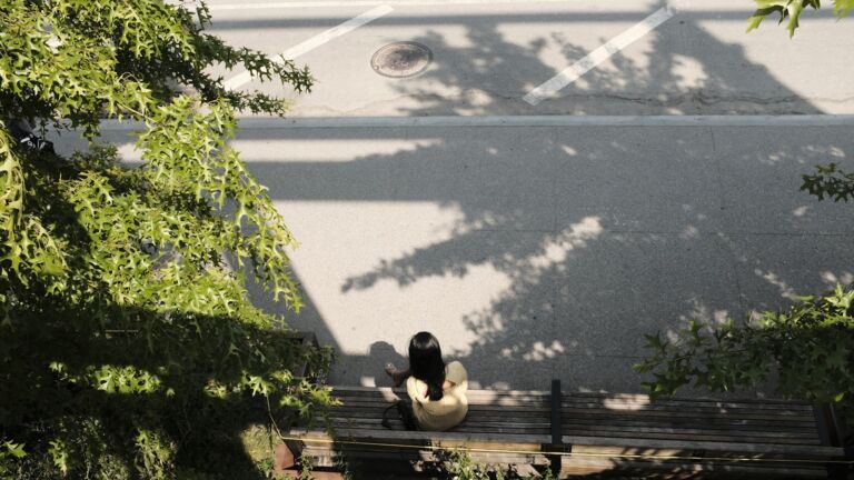 Person sitzt allein auf einer Parkbank im Baumschatten an einem heißen Sommertag
