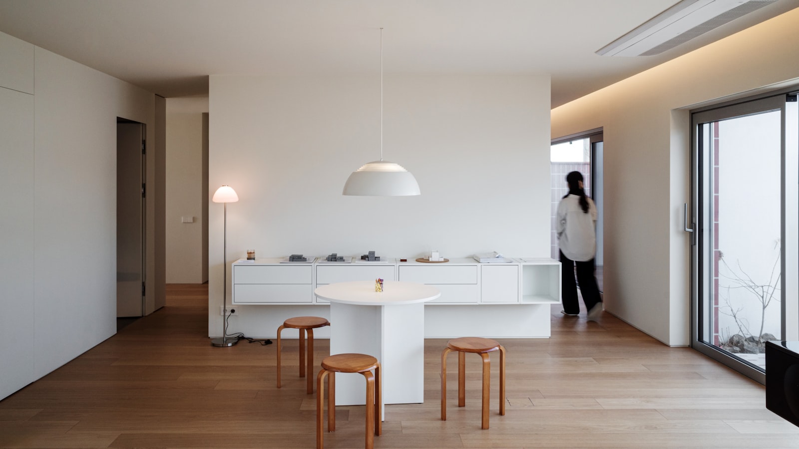 Helles, minimalistisch eingerichtetes Wohnzimmer mit weißen Möbeln, natürlichem Holzboden und großem Fenster