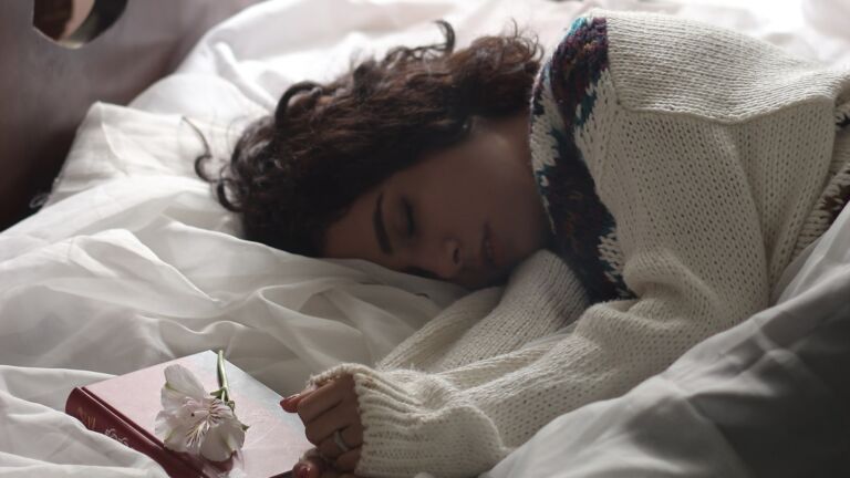 Frau schläft friedlich im Bett neben Blumen und einem Buch – tiefer, erholsamer Schlaf als Grundlage für Longevity