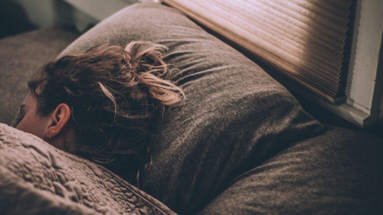 Frau schläft tief im Morgenlicht, Decke über das Gesicht gezogen – Schlafqualität und Erholung als Longevity-Faktor
