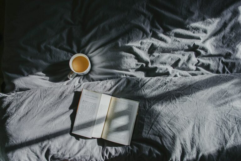 Weiße Keramiktasse neben aufgeschlagenem Buch auf grauem Textil – ruhiger Morgenmoment im Slow-Living-Alltag