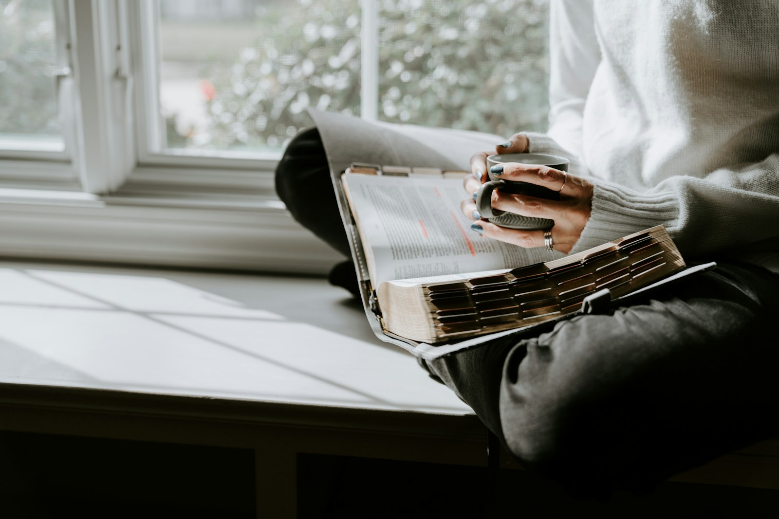 Person sitzt am Fenstersims und liest ein Buch – Slow Living Morgenritual