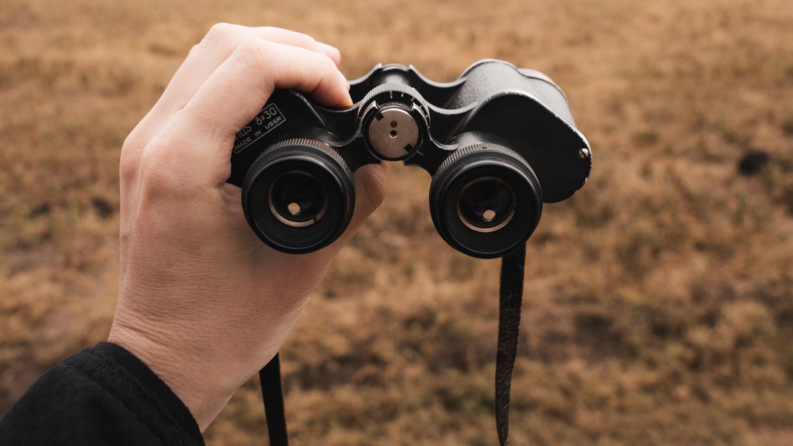Hand hält ein Fernglas mit Blick über eine weite Landschaft