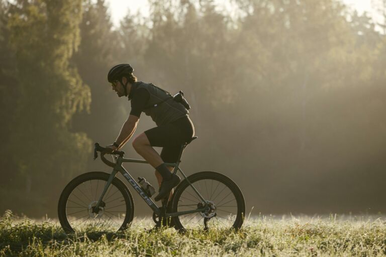 Radfahrer fährt mit einem Gravelbike durch eine grüne Wiesenlandschaft